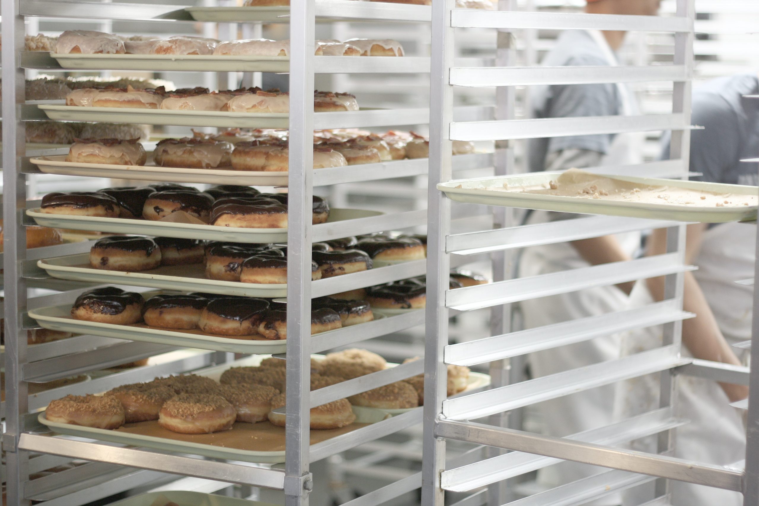 An image of donuts cooling on racks in the back of a franchise donut shop